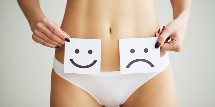 Woman Health Problem. Closeup Of Female With Fit Slim Body In Panties Holding White Card With Sad Smiley Face Near Her Stomach. Digestive Disorders, Period Pain, Health Issues Concept.